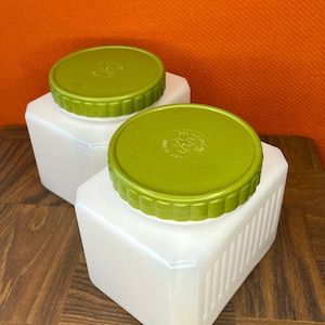 Puede incluir: Dos recipientes de plástico cuadrados blancos con tapas verdes. Las tapas tienen un diseño de panal de abeja en relieve y el texto "GEE PLASTICS INC. MADE IN USA" impreso en ellas.