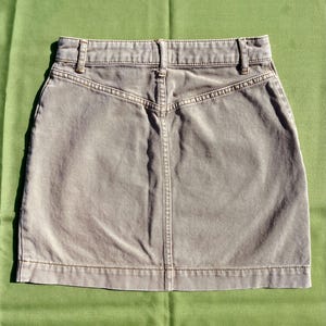 Puede incluir: Una falda vaquera color piedra con un dise&ntilde;o cl&aacute;sico. La falda presenta una cintura con trabillas, cierre de bot&oacute;n y cremallera, y costuras detalladas. La falda mide aproximadamente 40 cm de largo.
