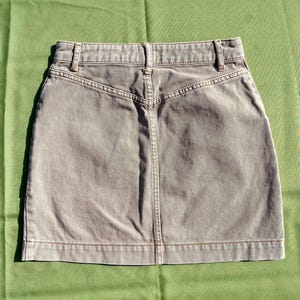 Puede incluir: Una falda vaquera color piedra con un dise&ntilde;o cl&aacute;sico de cinco bolsillos. La falda presenta una cintura alta, trabillas y un detalle de canes&uacute; trasero. La falda mide aproximadamente 40 cm de largo.