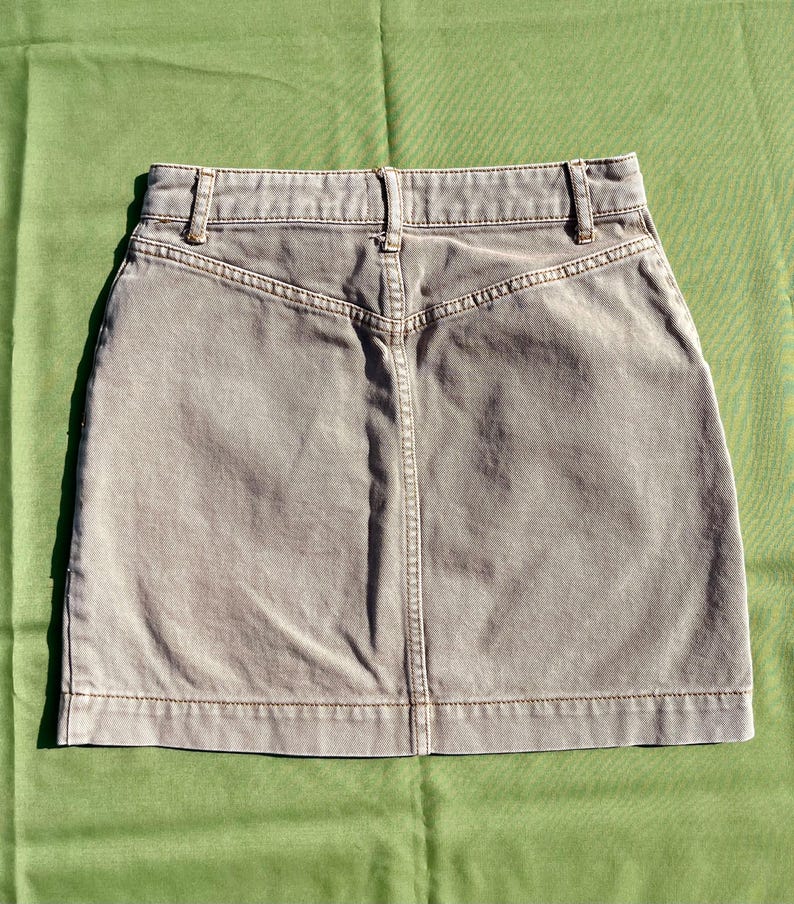Puede incluir: Una falda vaquera color piedra con un dise&ntilde;o cl&aacute;sico de cinco bolsillos. La falda presenta una cintura alta, trabillas y un detalle de canes&uacute; trasero. La falda mide aproximadamente 40 cm de largo.