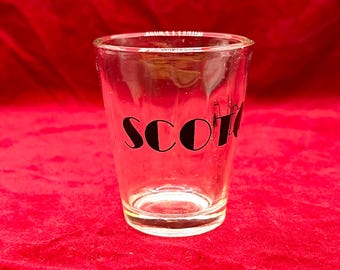 May include: A clear glass shot glass with the word "SCOTCH" printed in black on the front.