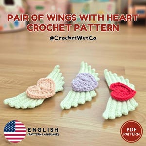 Könnte beinhalten: Drei gehäkelte Flügel mit herzförmigen Zentren in Rosa, Lila und Rot. Die Flügel sind hellgrün, und der Text "PAIR OF WINGS WITH HEART CROCHET PATTERN" wird angezeigt. Das Muster ist auf Englisch.