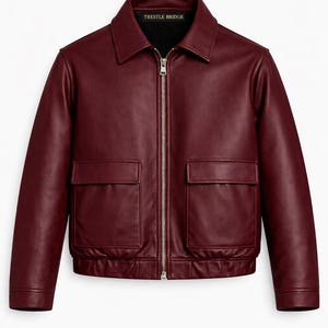 May include: A burgundy leather jacket with a collared neckline and a silver zipper. The jacket has two front pockets and the text "Trestle Bridge" is visible on the collar.