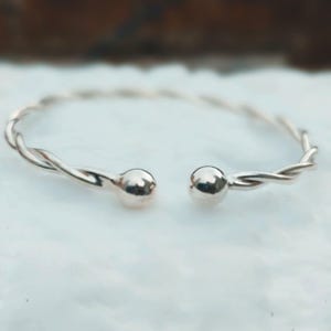 Può includere: Un bracciale a polsino color argento con un design a torsione. Il bracciale ha una finitura lucida e presenta una piccola sfera rotonda ad ogni estremità aperta. Il bracciale è progettato per essere indossato al polso.