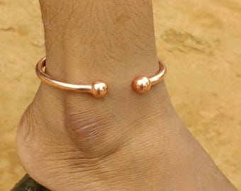May include: A polished copper anklet featuring a smooth, open-ended circular band design. The ends of the anklet are finished with two rounded, spherical ball terminals that face each other, creating a simple and clean aesthetic for the ankle.