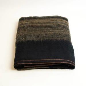 May include: Folded blanket with a color gradient from brown to black. The top section is a fuzzy brown, transitioning to a solid black at the bottom. The blanket has a brown stitched border.