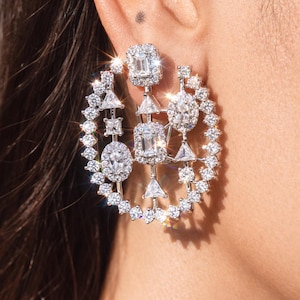 May include: A dazzling, geometric earring design featuring a circular arrangement of sparkling, clear gemstones. The earrings showcase a mix of shapes, including squares, triangles, and round stones, creating a luxurious and eye-catching accessory.