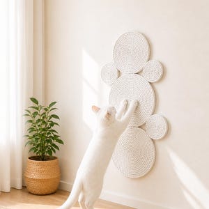 White cat stretching against a light natural jute wall-mounted scratching mat in a bright minimalist living room.