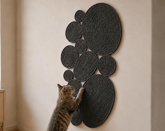 Könnte beinhalten: Ein wandmontierter Kratzbaum für Katzen, bestehend aus mehreren dunkelgrauen, kreisförmigen Scheiben unterschiedlicher Größe, die in einer Gruppe angeordnet sind. Die Scheiben bestehen aus fest gewickeltem Seil mit strukturierter Oberfläche.