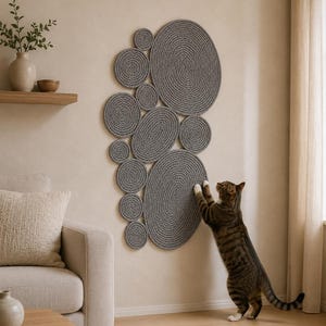May include: A wall-mounted cat scratching post consisting of multiple circular and oval gray rope-coiled pads arranged in a cluster. A brown tabby cat stands on its hind legs, reaching up to scratch the surface of the largest lower oval pad.