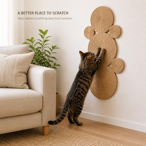 K&ouml;nnte beinhalten: Ein wandmontierter Kratzbaum f&uuml;r Katzen aus beigefarbenem, spiralf&ouml;rmig gewickeltem Seil in kreisf&ouml;rmiger Anordnung. Eine getigerte Katze kratzt an der Oberfl&auml;che. Der Text an der Wand lautet: A BETTER PLACE TO SCRATCH. Helps redirect scratching away from furniture.