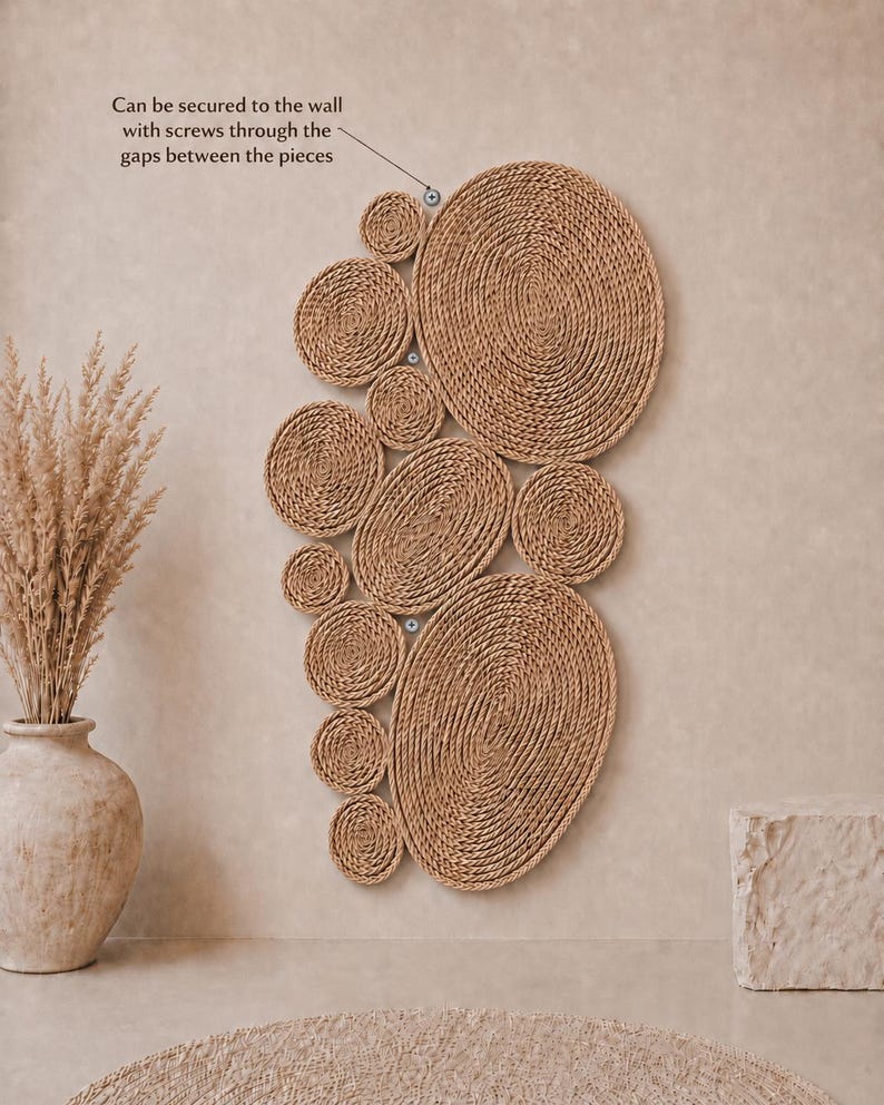 May include: A wall-mounted art piece composed of multiple circular and oval shapes made from coiled tan rope. The text states: Can be secured to the wall with screws through the gaps between the pieces. The design features varied sizes.