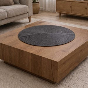 Pode incluir: Um lugar americano circular cinza-escuro com uma textura de corda enrolada firmemente. O lugar americano apresenta um padrão espiral concêntrico uniforme que irradia do centro para a borda externa, criando um design plano e redondo.