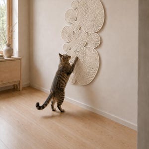 May include: A wall-mounted cat scratching post consisting of multiple circular pads made of coiled off-white rope. The pads are arranged in a cluster of varying sizes, featuring a textured surface for scratching, mounted directly onto a flat wall.
