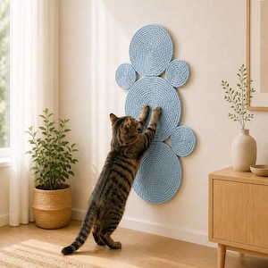 K&ouml;nnte beinhalten: Ein an der Wand montierter Kratzbaum f&uuml;r Katzen, bestehend aus mehreren hellblauen, seilumwickelten Kreisen unterschiedlicher Gr&ouml;&szlig;e, die in einer vertikalen Gruppe angeordnet sind. Die texturierten Scheiben bieten eine Kratzfl&auml;che.
