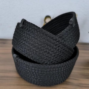 Puede incluir: Dos cestas negras tejidas, apiladas una encima de la otra. Las cestas tienen un aspecto texturizado y una forma redondeada. Están hechas de un material oscuro y probablemente se utilizan para almacenamiento o decoración.