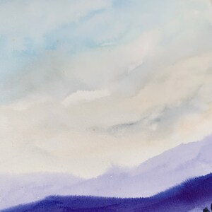 May include: Watercolor landscape art print featuring a serene mountain scene. The artwork showcases a gradient of colors, with a light blue sky, soft white clouds, and layers of purple mountains. The bottom of the print has dark trees. The text "Somerset Velvet Giclee" is visible.