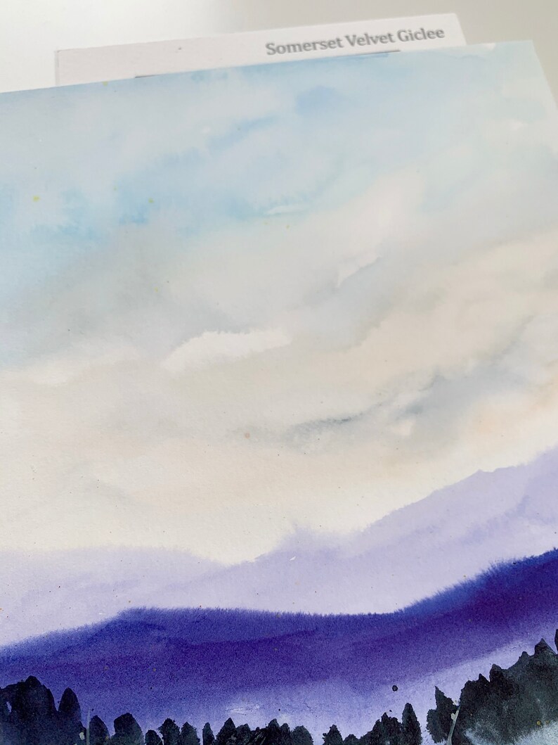 May include: A watercolor painting of a purple mountain range with a light blue sky and white clouds. The painting is on a white background.
