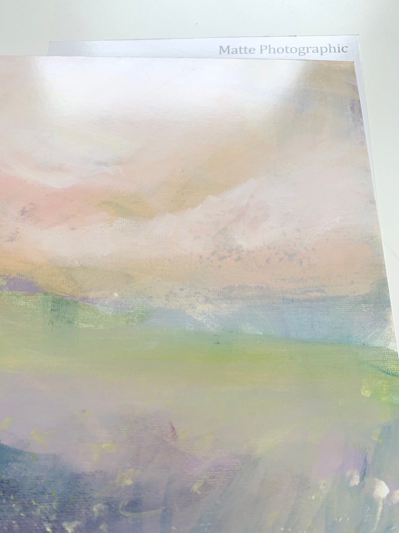 May include: Abstract painting with a soft, dreamy landscape. The painting features a light pink and yellow sky with white clouds, a green field, and a purple and blue foreground. The painting has a textured surface and a matte finish.