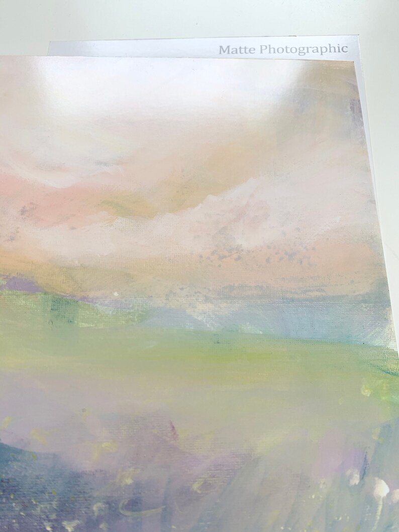 May include: An abstract landscape painting with soft pastel colors. The artwork features a blend of pink, beige, green, and purple hues, creating a serene and dreamy atmosphere. The words "Matte Photographic" are printed on the top edge of the artwork.
