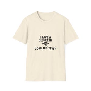 Op de afbeelding: Crèmekleurig T-shirt met de zwarte tekst "I HAVE A DEGREE IN GOOGLING STUFF". Het ontwerp bevat een afstudeerhoed en een vergrootglas. Het shirt is gemaakt van een zacht materiaal.