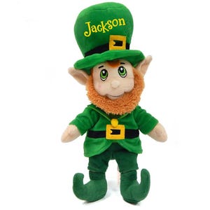 May include: A plush leprechaun doll wearing a green outfit and hat with the name "Jackson" embroidered on it. The doll has a red beard, rosy cheeks, and green eyes. The hat has a gold buckle.