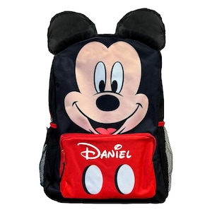 May include: Black backpack featuring Mickey Mouse's face with 3D ears. The red front pocket has the name "Daniel" printed on it, along with two white circles. The backpack has black mesh side pockets and red accents.