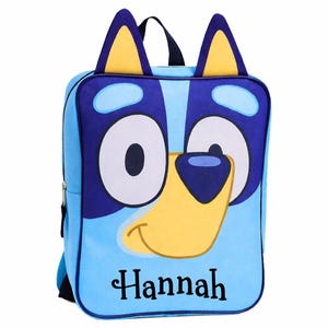 May include: A light blue backpack featuring a cartoon dog face with large eyes, a yellow snout, and blue ears. The backpack has a zipper closure and a top handle. The name "Hannah" is printed in black script on the front.