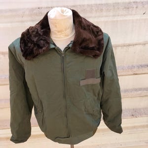 Peut inclure: Une veste vert olive dotée d'un col en fausse fourrure marron foncé, d'une fermeture éclair frontale intégrale et d'un écusson rectangulaire sur la poitrine gauche. La veste comprend des manches longues avec poignets et un bas ourlé.