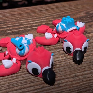May include: Two articulated flamingo figures in bright pink with black beaks and white eyes. One flamingo carries a blue and white striped inner tube, while the other features a blue and white beach ball and a small blue castle structure on its back.