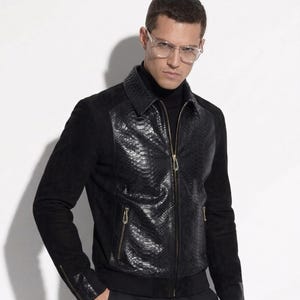 Könnte beinhalten: Eine schwarze Jacke mit einer strukturierten Vorderseite in Schlangenlederoptik, Ärmeln und Rücken aus Wildleder, einem klassischen Kragen sowie goldfarbenen Metallreißverschlüssen an der Front, den Seitentaschen und den Ärmelbündchen.