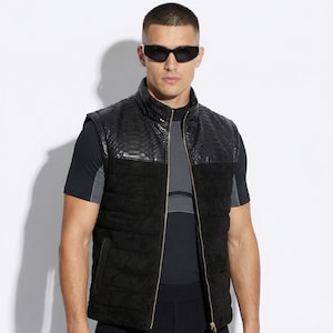 May include: Black quilted vest with a snakeskin-textured yoke and collar, featuring a gold zipper. The vest is paired with a black t-shirt and black pants. The model is wearing black sunglasses.