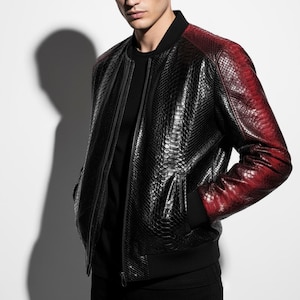May include: Black bomber jacket with red ombre sleeves. The jacket features a textured, snake-skin pattern, a black ribbed collar, cuffs, and hem, and a front zip closure. The jacket has two front pockets.