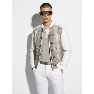 Op de afbeelding: Een witte bomberjack met slangenpatroon en witte mouwen. De jas wordt gecombineerd met een witte broek en een grijs overhemd. De persoon op de foto draagt een zonnebril.