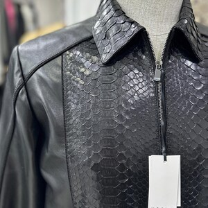 Peut inclure: Veste en cuir noir avec un panneau textur&eacute; en peau de serpent sur le devant et le col. La veste a une fermeture &eacute;clair et une &eacute;tiquette qui indique "ISSLA". La veste est pr&eacute;sent&eacute;e sur un mannequin.