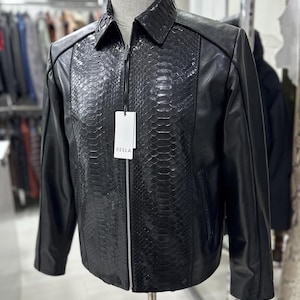 Peut inclure: Une tasse en c&eacute;ramique blanche avec une anse noire et le texte "But First, Coffee" en noir, dans une police manuscrite. La tasse est pos&eacute;e sur une surface blanche.