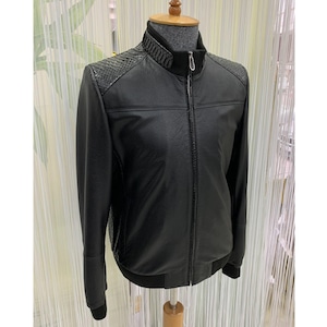 Op de afbeelding: Zwarte leren jas met een opstaande kraag en een ritssluiting. De jas heeft getextureerde panelen op de schouders en een geribbelde gebreide kraag en manchetten. De jas wordt op een mannequin getoond.