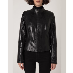May include: A black leather jacket with a snakeskin pattern. The jacket has a high collar and a full-length zipper. The sleeves are long, and the jacket is fitted. The model is wearing black pants.