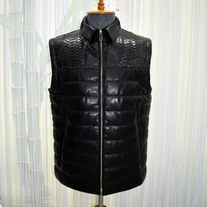 May include: A black leather vest with a quilted design and a reptile-textured collar. The vest has a full-length gold zipper and is displayed on a mannequin. The vest is a stylish outerwear garment.