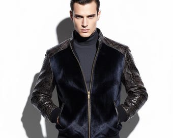 May include: A navy blue bomber jacket with a fur-like texture on the front and snake-skin patterned sleeves and shoulder accents. The jacket has a gold zip and black ribbed cuffs and hem. The model is wearing a dark grey roll neck.