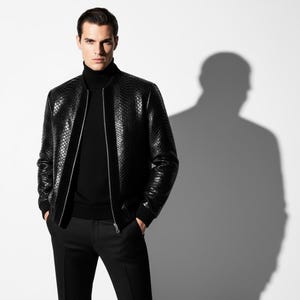 May include: A black leather bomber jacket with a reptile skin texture, worn over a black turtleneck and black trousers. The jacket has a silver zip and a sleek, modern design. The image is set against a white background with a shadow.