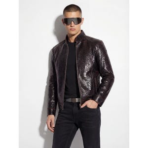 May include: A dark brown leather jacket with a snakeskin texture. The jacket has a zipper closure and a stand-up collar. The model is wearing black jeans and sunglasses.