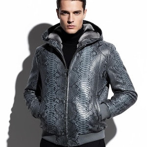 May include: A hooded, gray snakeskin-patterned jacket with a zipper closure. The jacket has a gray fur-lined hood and gray ribbed cuffs and hem. The person in the image is wearing a black turtleneck.