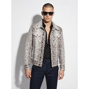 Könnte beinhalten: Eine Jacke mit Schlangenmuster mit zwei Brusttaschen und einem Kragen. Die Jacke ist in Grau-, Braun- und Weißtönen gehalten. Die Person trägt ein schwarzes Hemd und eine Sonnenbrille. Die Hose ist marineblau.