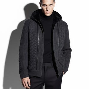 Könnte beinhalten: Dunkelgrauer Kapuzenpullover mit Reißverschluss und Zopfmuster. Der Pullover hat ein schwarzes Kunstfellfutter in der Kapuze und einen schwarzen Rollkragenpullover. Das Model trägt eine schwarze Hose.