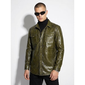 Op de afbeelding: Een olijfgroen overhemd met knopen en een slangenpatroon. Het overhemd heeft twee borstzakken en wordt gedragen over een zwarte coltrui. De persoon draagt een zwarte zonnebril en een zwarte broek.