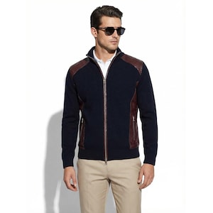 Peut inclure: Un pull zippé bleu marine avec des empiècements et des accents en cuir marron. Le pull a un col montant et deux poches avant. La personne porte des lunettes de soleil et un pantalon beige.