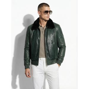 May include: A dark green leather bomber jacket with a black fur collar. The jacket features a snakeskin-like pattern on the front and is paired with a light brown polo shirt and white pants. The person is wearing sunglasses.