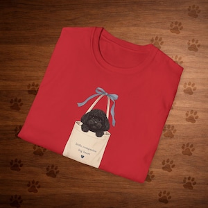 Könnte beinhalten: Ein rotes T-Shirt mit einer Grafik eines schwarzen Hundes in einer weißen Tragetasche mit einer blauen Schleife. Die Tragetasche trägt den Text "little companion big heart" und ein blaues Herz. Das Shirt ist aus weichem Material.