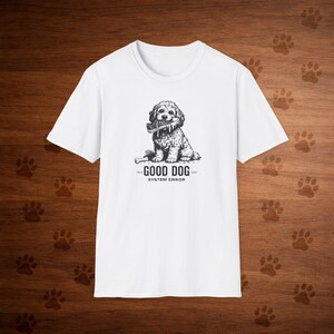 May include: White t-shirt with a black and white illustration of a dog holding a shoe. The text "GOOD DOG" and "SYSTEM ERROR" are printed below the dog image. The t-shirt is made of cotton.